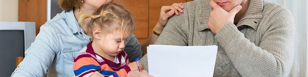 Father holding bills while mother comforts him by placing her hand on his shoulder while also holding child.