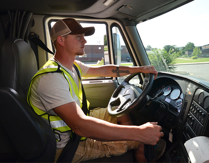 Male student inside the cab wearing reflective vest and shifting gears.