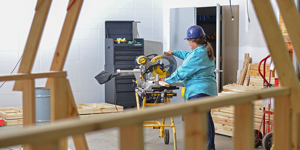 Student using a miter saw to cut a 2x4 for framing project in the foreground.