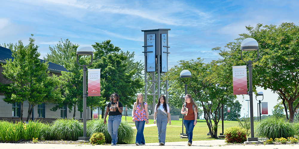 Four students walking through campus as a group with the commemorative clock tower in the background.