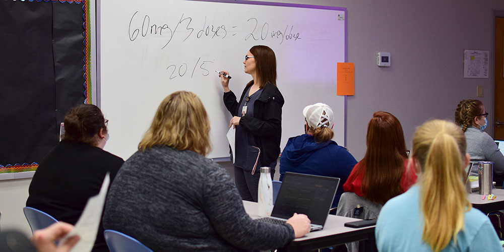 Medical Surgical I instructor writing medication dosage on whiteboard while students at their desks pay attention.