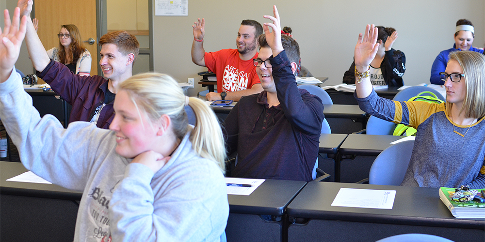 Classroom with several students who have their hands raised.