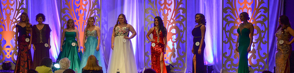 Contestants posing on stage with lighted curtain backdrop